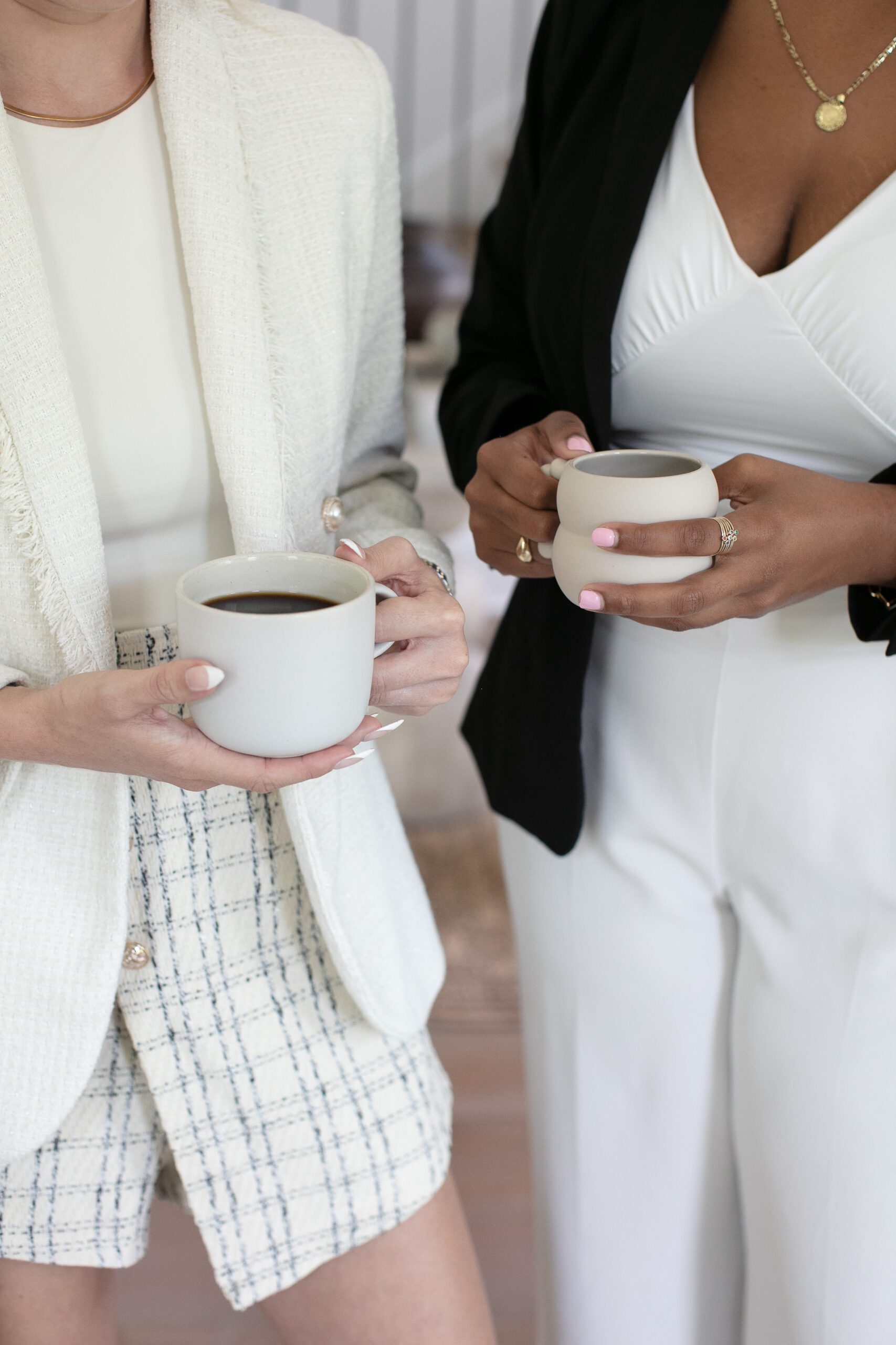 Two women in business attire stand next to each other while holding mugs of coffee