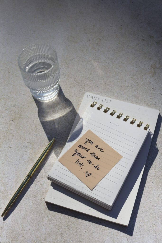 A notepad that says "you are more than your to do list" next to a glass of water. 